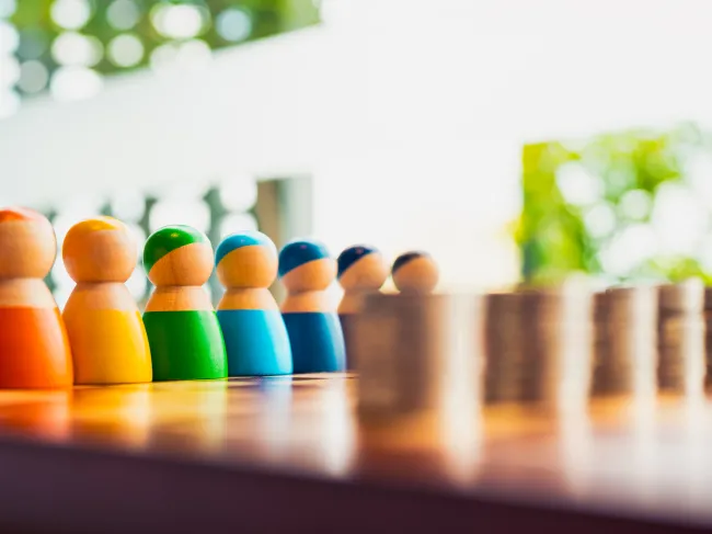 Colorful wooden figures lined up in front of coin stacks